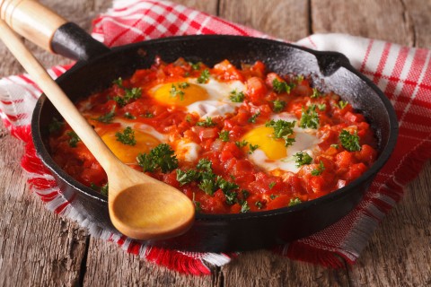 Homemade breakfast shakshuka of fried eggs with tomato close-up.